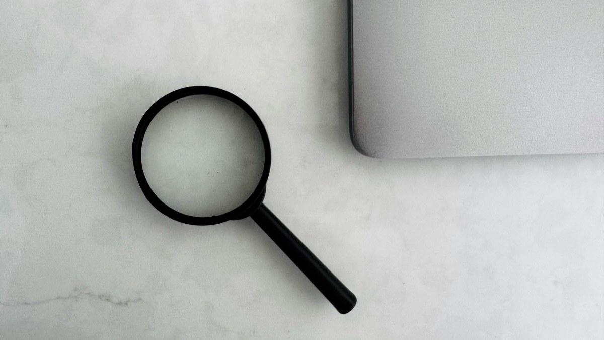 Profissional analisando documentos de marca com lupa em ambiente de trabalho focado